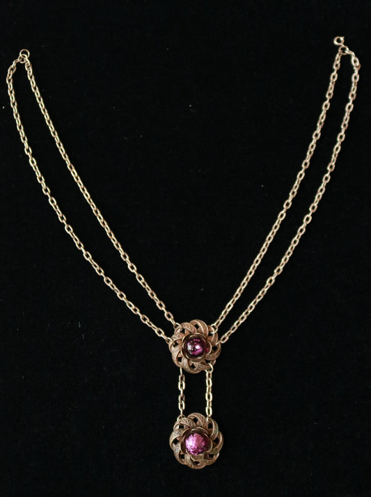 Vintage floral drop necklace with two ornate metal flower motifs set with purple Murano glass cabochons on a black velvet background.