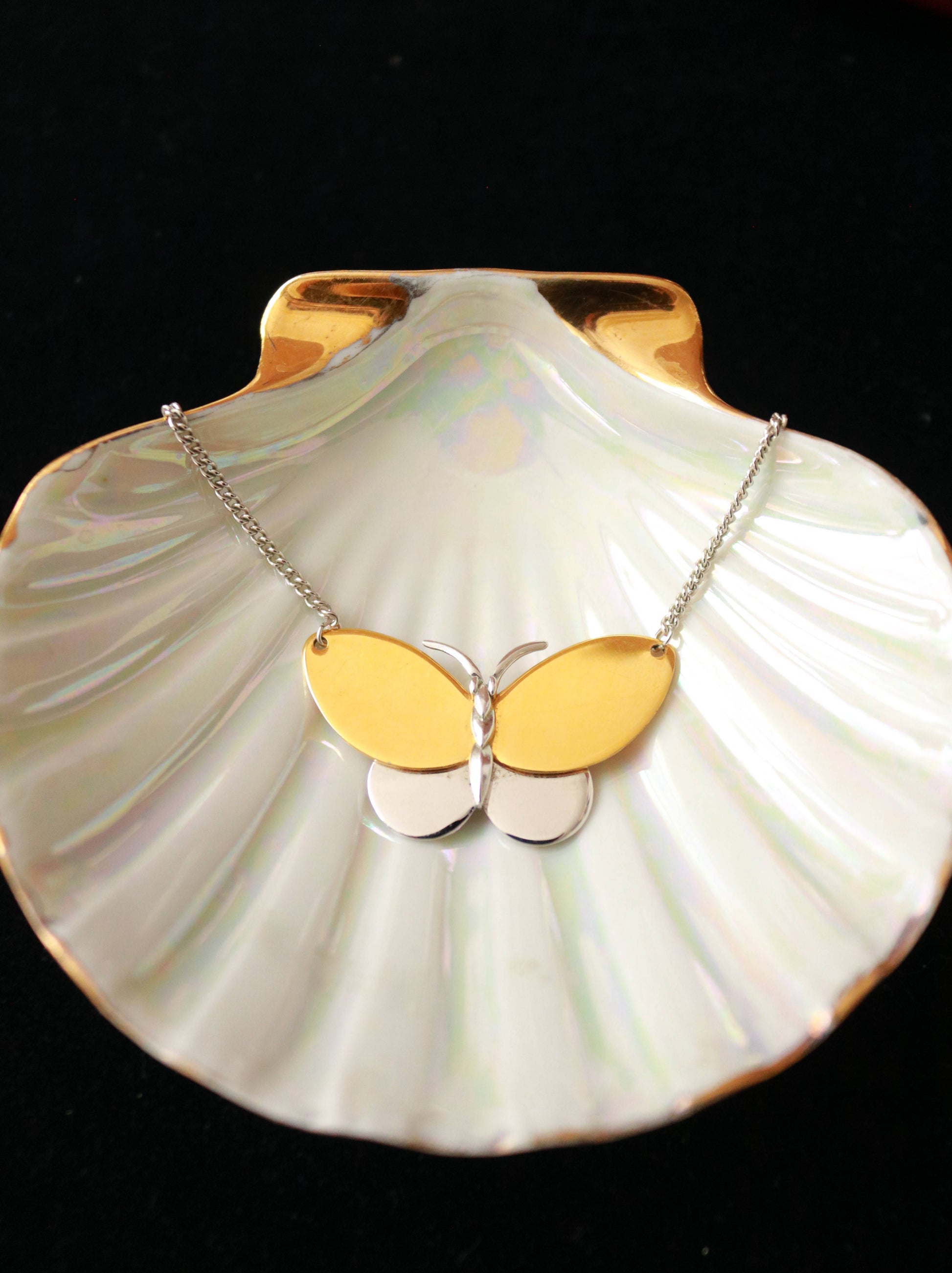 Vintage AVON two-tone butterfly pendant necklace with gold-plated wings and silver-tone details on a black velvet background.