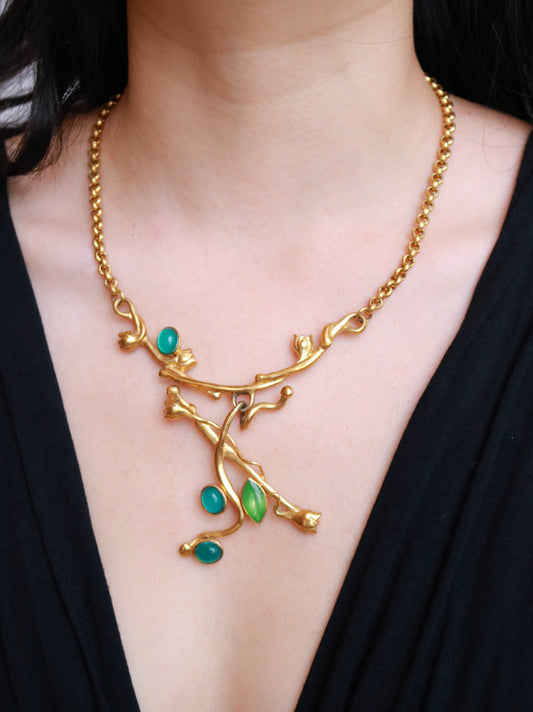 Vintage MICRIS botanical statement necklace worn to showcase its sculptural gold-tone design and green cabochons.