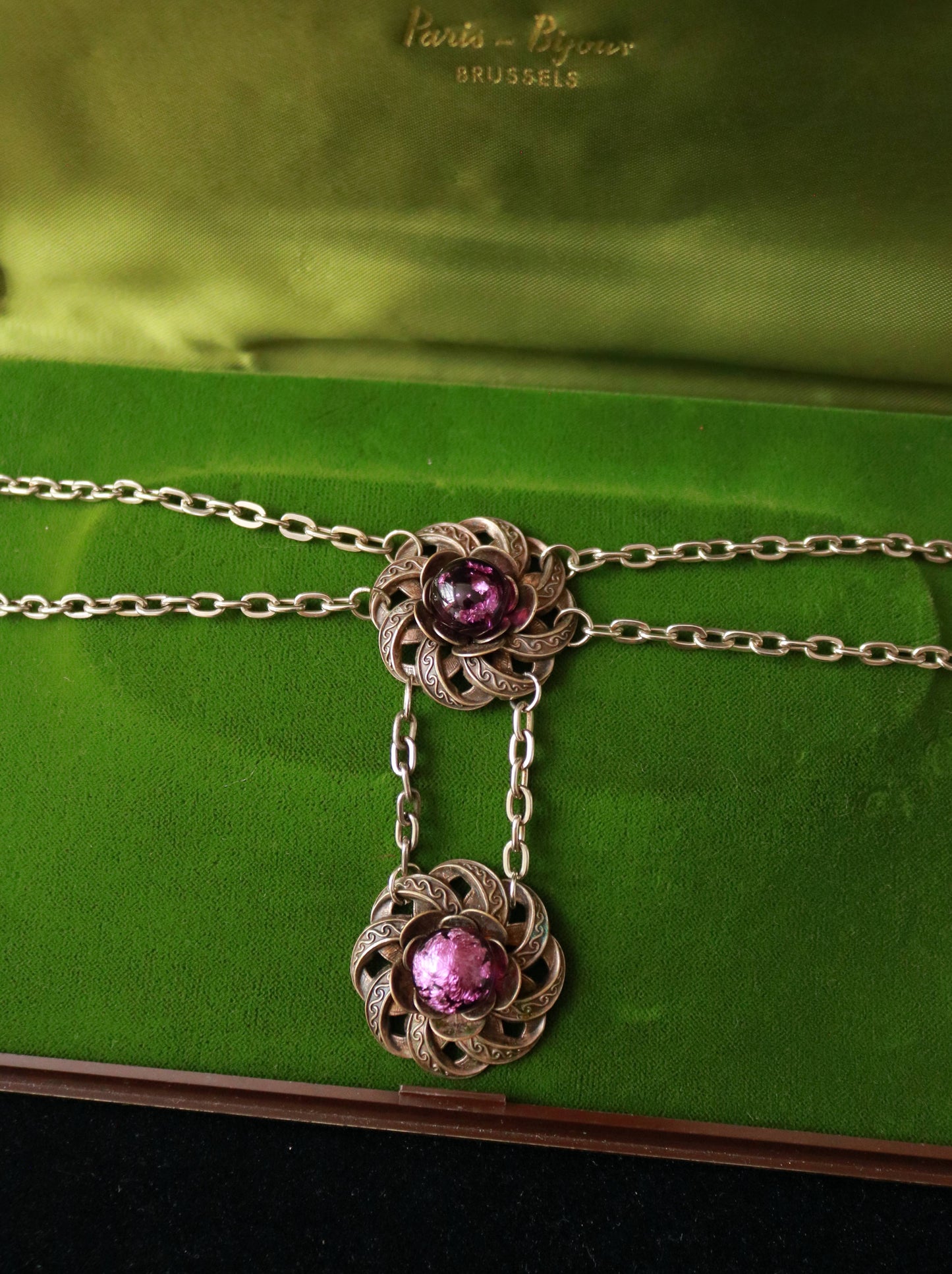 Close-up of an ornate vintage floral necklace featuring luminous purple Murano glass cabochons and detailed metalwork.