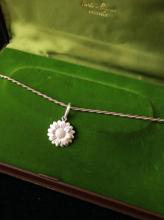 Close-up of a vintage daisy pendant featuring sculpted petals and a textured floral centre.