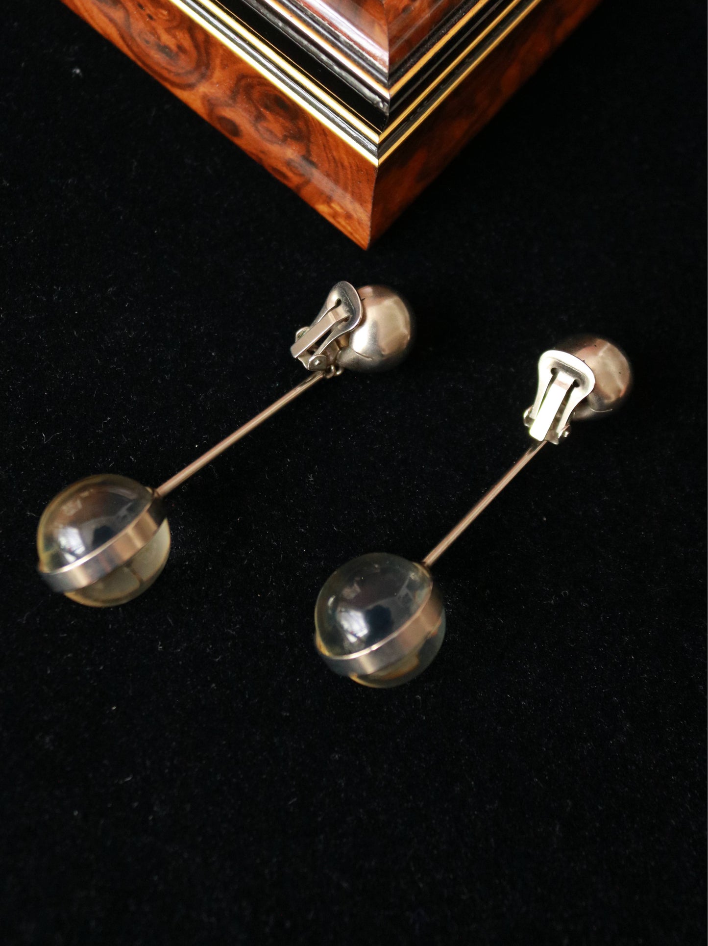 Close-up of 1970s vintage clip-on earrings featuring polished silver-tone spheres and translucent resin ball drops.