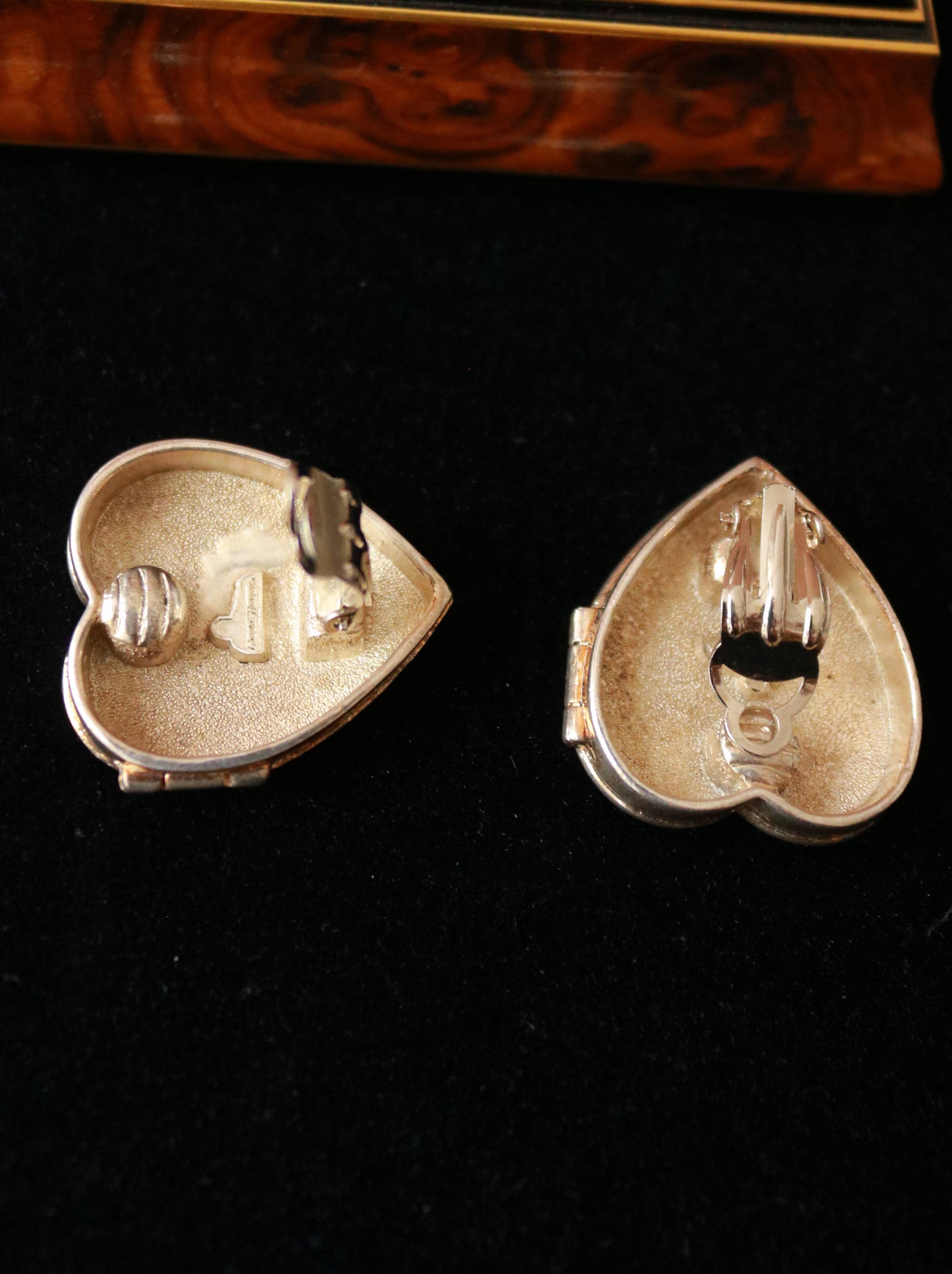 Close-up of Chantal Thomass clip-on earrings featuring a polished heart-shaped box design and decorative monogram.