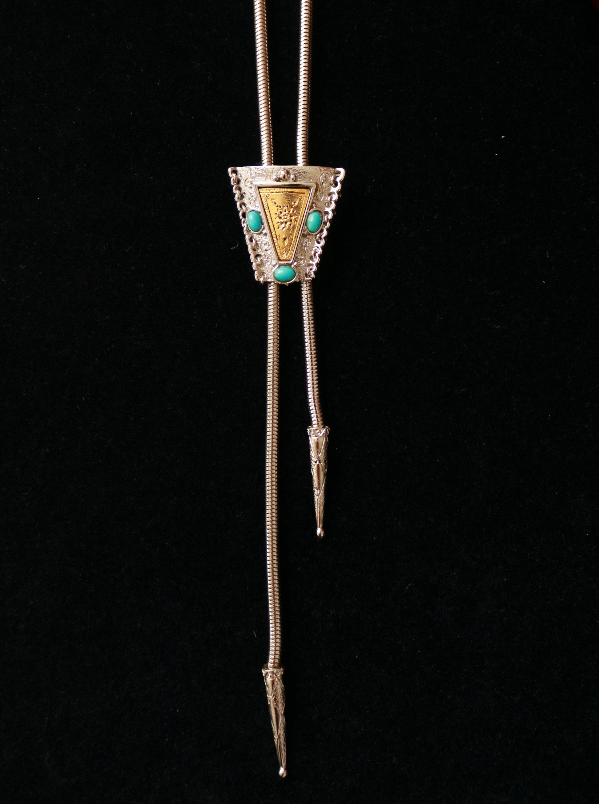 Close-up of a vintage bolo necklace featuring an ornate triangular adjustable slider with turquoise-tone cabochons.