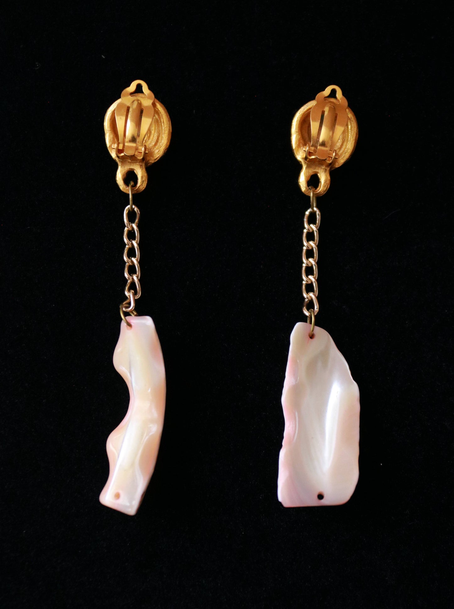 Close-up of vintage long clip-on earrings featuring sculptural gold-tone spiral clips and natural shell drops.