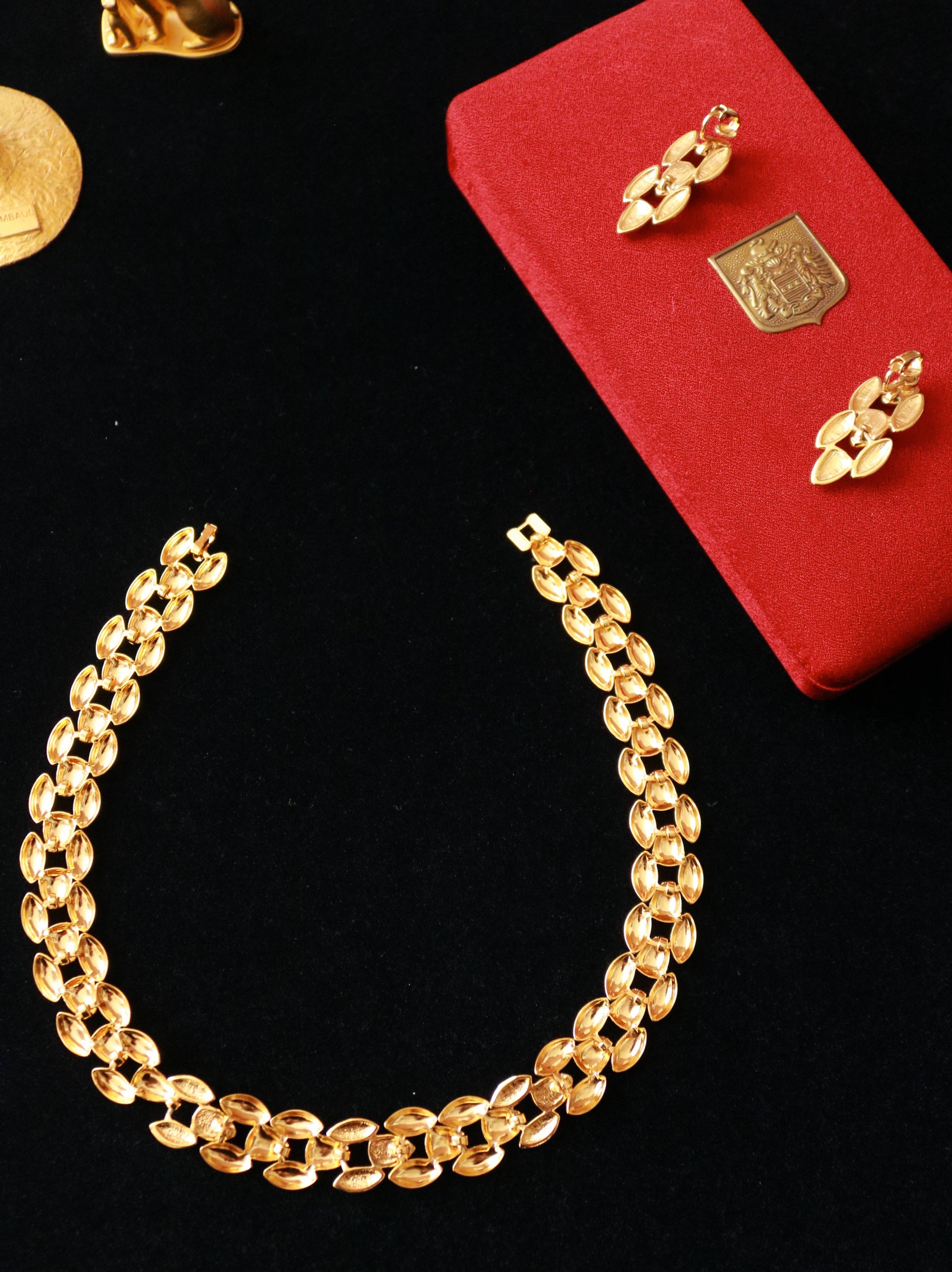 Close-up of vintage gold-tone necklace with sculptural links and red cabochon accents.