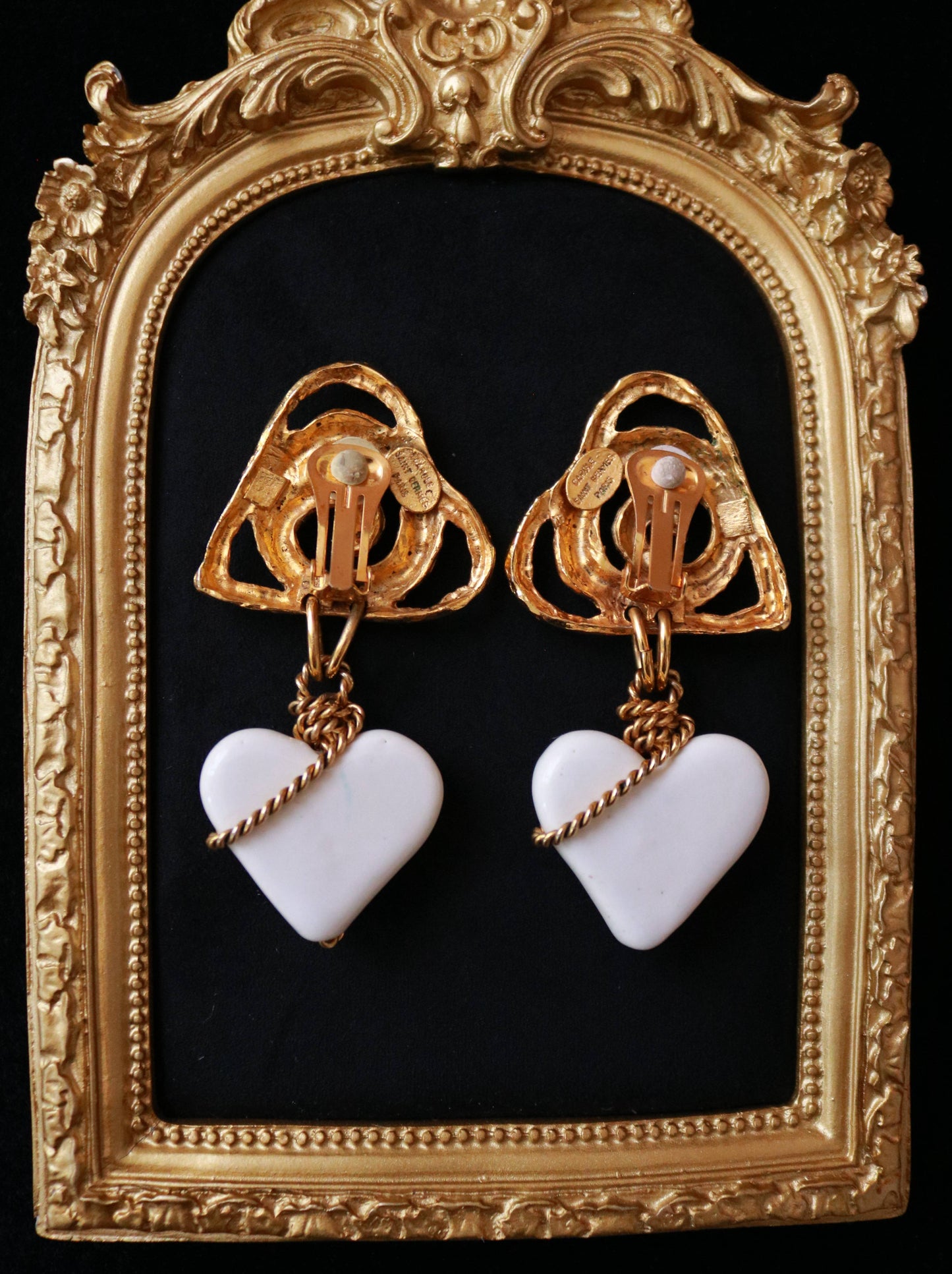 Close-up of signed Carole Saint Germès 24K gold plated clip-on earrings featuring sculptural heart motifs and white heart drops.