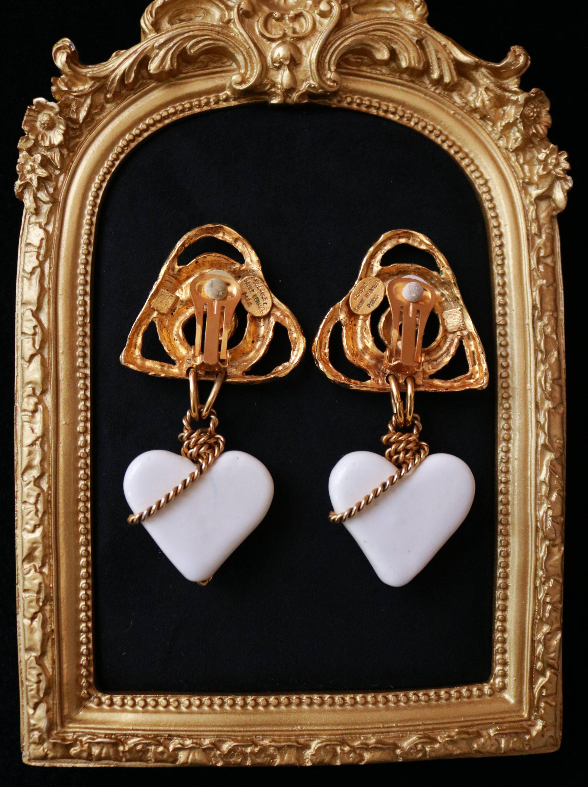 Close-up of signed Carole Saint Germès 24K gold plated clip-on earrings featuring sculptural heart motifs and white heart drops.